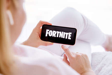 Riga, Latvia - March 26, 2021: Woman holding phone with Fortnite logo on the screenのeditorial素材