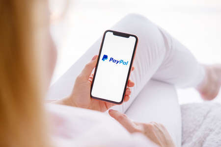 Riga, Latvia - March 26, 2021: Woman holding phone with PayPal logo on the screenのeditorial素材
