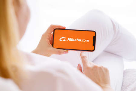 Riga, Latvia - March 26, 2021: Woman holding mobile phone with Alibaba logo on the screenのeditorial素材