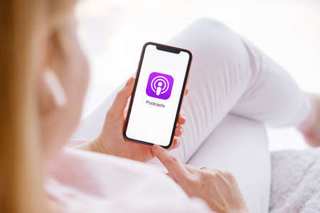 Riga, Latvia - March 26, 2021: Woman holding phone with Podcasts icon on the screenのeditorial素材