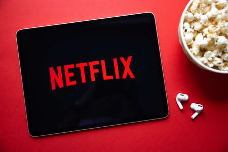 Riga, Latvia - April 14, 2021: Netflix logo on iPad with popcorn and wireless earbuds.のeditorial素材