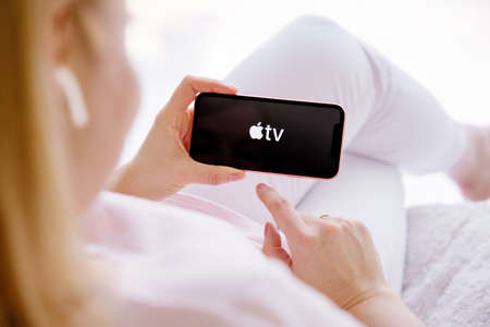 Riga, Latvia - March 26, 2021: Woman holding phone with Apple TV logo on the screenのeditorial素材