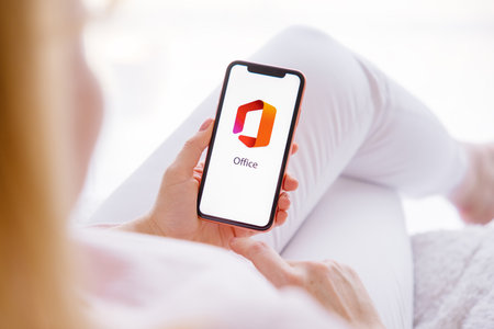 Riga, Latvia - March 26, 2021: Woman holding mobile phone with Office logo on the screenのeditorial素材