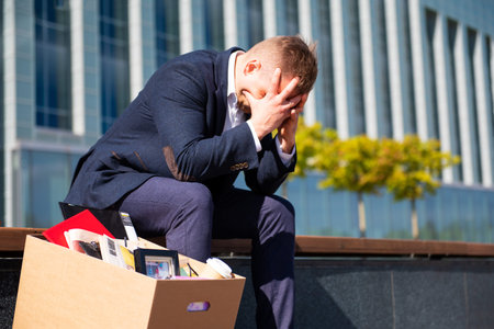 Depleated former employee sitting with his belongings stuffed in a box next to him.