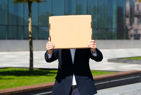 Young professional standing at office building and holding empty cardboard signの写真素材