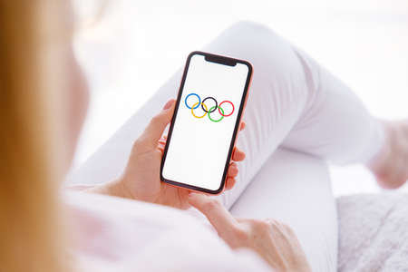 Riga, Latvia - March 26, 2021: Woman holding mobile phone with Olympic Rings on the screenのeditorial素材