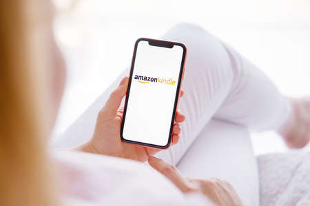 Riga, Latvia - March 26, 2021: Woman holding mobile phone with Amazon Kindle logo on the screenのeditorial素材