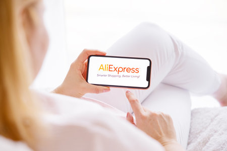 Riga, Latvia - March 26, 2021: Woman holding mobile phone with AliExpress logo on the screenのeditorial素材