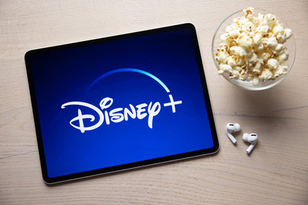 Riga, Latvia - April 14, 2021: Disney+  logo on iPad with popcorn and wireless earbuds.のeditorial素材