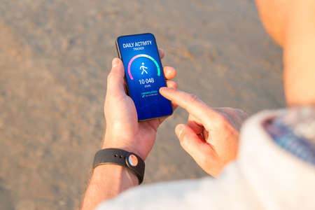 Man using daily activity tracking app on mobile phone showing 10 000 steps daily goal achievementの写真素材