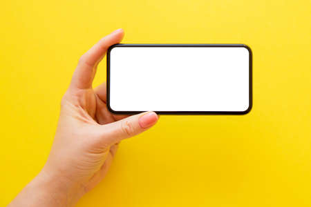Mobile phone with empty white screen in horizontal orientation on yellow backgroundの写真素材