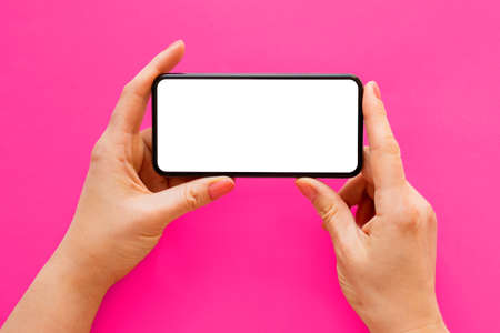Mobile phone with empty white screen held in hands horizontally on bright pink backgroundの写真素材