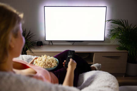 Woman watching TV at home, empty white TV screen mockupの写真素材