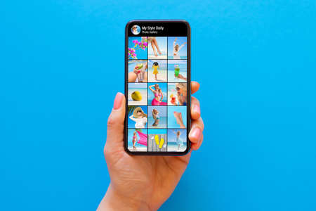 Someone's photo gallery on social media shown on the screen of mobile phone on blue backgroundの写真素材