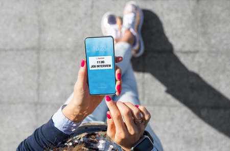 Woman holding mobile phone and looking at pop-up notification reminding of job interviewの写真素材