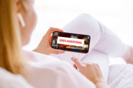 Concept of video marketing, woman looking at ad banner while watching videos online on her phoneの写真素材