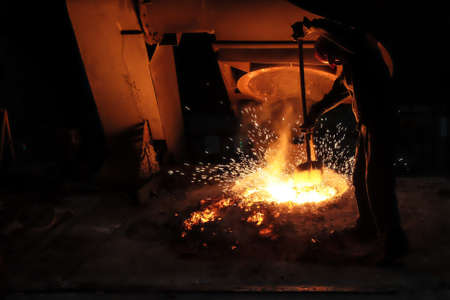 Foundry worker collecting molten metal sample for testing with sparks flying.の写真素材