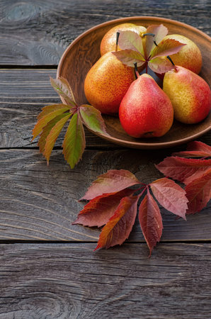 Pears in a clay bowl. Dark wooden background in rustic style. Autumn leaves.の写真素材