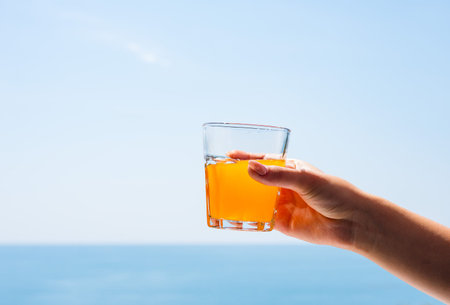 A glass of juice in a woman's hand. A glass of juice against the background of the sea.