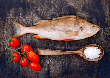 Fresh raw fish on a dark wooden background. River perch and spicesの写真素材