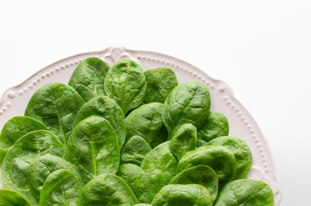 Young leaves of spinach on a plate. Top view, white background, copy space. Detox, a dietary food...