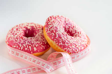 Measuring tape and pink donuts on a white background. The concept of dietの写真素材