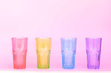 Four identical glass glasses: red, green, blue, purple. Four multicolored glass cups for drinks on a pink background. Close-upの写真素材