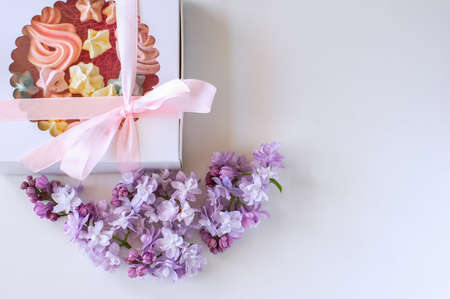 Homemade marshmallows of different colors are beautifully packaged in a gift box. White background, blooming lilac. Close-upの写真素材