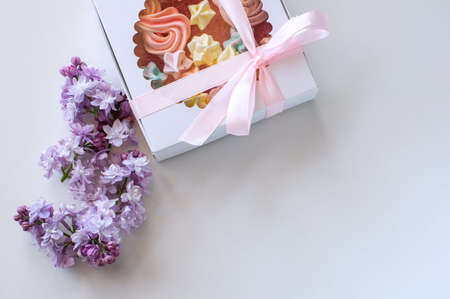 Homemade marshmallows of different colors are beautifully packaged in a gift box. White background, blooming lilac. Close-upの写真素材