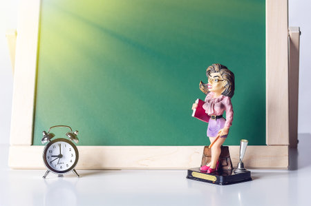 Back to school. Alarm clock and the figure of the teacher on the background of the blackboard....