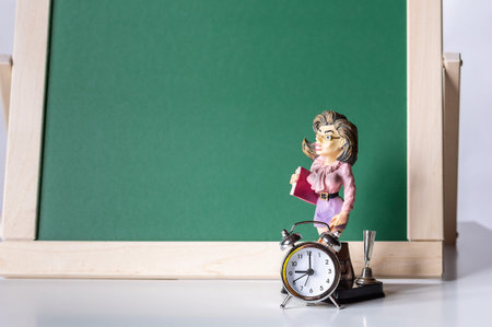 Back to school. Alarm clock and the figure of the teacher on the background of the blackboard....