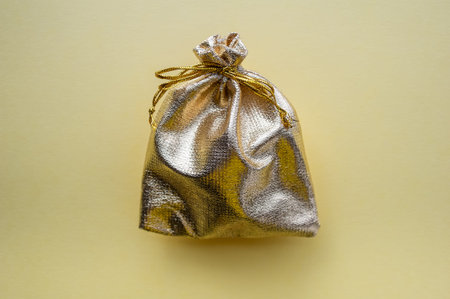 Gift bag of golden fabric on a yellow background. The concept of the holiday. View from above.