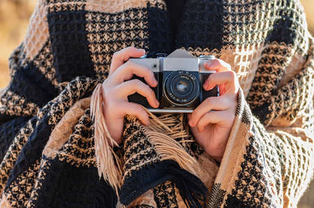 Outdoor photoshoot. The girl is wrapped in a warm checkered plaid and is holding a vintage camera in her hands. Close up.の写真素材