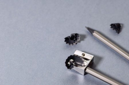 Two gray wooden pencils, metal sharpener and shavings on a gray background. The concept of...