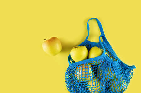 Blue string bag with apples lies on a yellow background. Flat lay.の写真素材