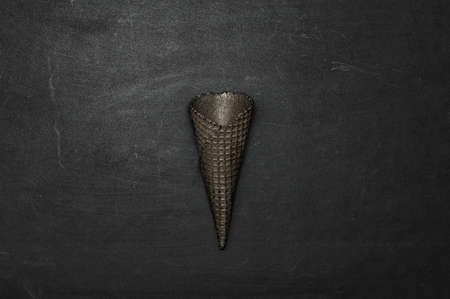 Empty black ice cream cone on a black background, minimalistic concept. Dark background. Copy space. Close up. Flat lay.の写真素材