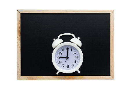 White alarm clock on the background of a black school board. The concept of the beginning of the...