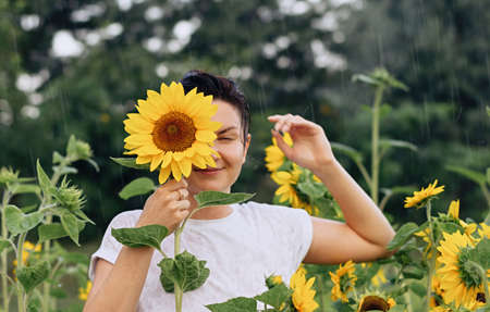 A young girl stands in the summer rain in a field with sunflowers. Happiness and slow-down concept.の写真素材