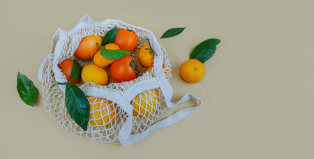 White string bag with orange fruits. Ripe persimmons, tangerines and grapefruit close-up. Flat lay, copy space.の写真素材