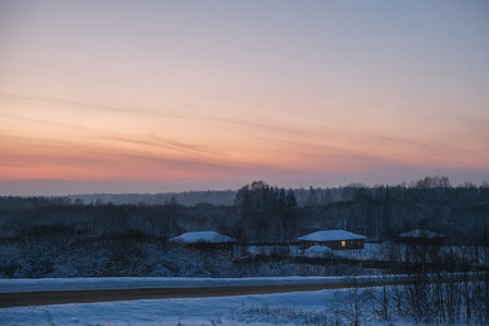 Picturesque winter sunset casts pastel colors across a rural village. Snowy houses, tranquil sky, and forest silhouettes create serene landscape for seasonal nature, peaceful environment or countryside concept.の写真素材