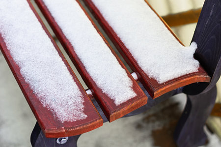 Closeup of a wooden bench covered with fresh snow outdoors in winter. Chilly texture, empty seat, rest and solitude concept in park, urban or backyard environment. Perfect for seasonal design.の写真素材