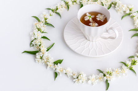 A white porcelain cup filled with fragrant herbal jasmine tea. The scene is artfully decorated with fresh jasmine flowers arranged in a graceful circle, conveying serenity and natural luxury.の写真素材