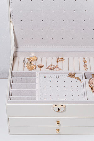 Close up of a cream jewelry box with neatly organized gold rings, earrings and necklace on soft compartments, stylish minimalist accessory storage on white background.の写真素材