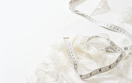White lace trim beside a measuring tape on a bright white background. Clean flatlay for sewing and...