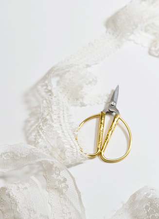 Delicate white lace ribbon with vintage gold embroidery scissor on a clean white background. Minimal...