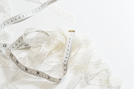 White lace ribbon and measuring tape arranged on a white background. Minimal sewing and dressmaking concept with copy space for atelier branding, diy tutorials, bridal design, and lingerie.の写真素材