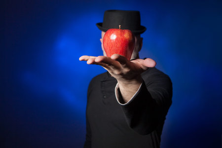 The man covered his face with an apple. The apple lies on the palm of your hand. A man in black...