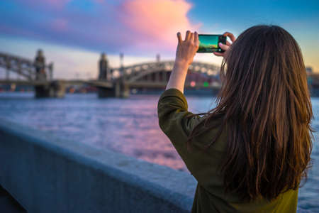Tourist in St. Petersburg. Girl tourist takes pictures on the phone. Bolsheokhtinsky Bridge. Bridges of Petersburg. Russia.の写真素材