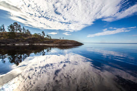 The clouds are reflected in the lake. The stones go into the water. Horizon on the water. Wild nature. Islands on the Ladoga lake. Karelia. Ladoga lake. Russia. The nature of Karelia.の写真素材