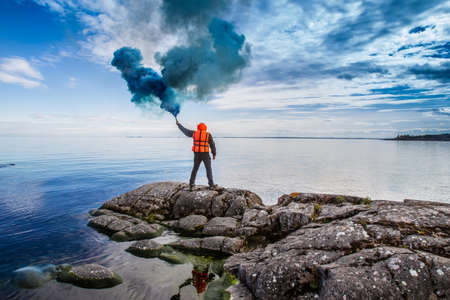 A man is waiting for help. The man stands on the chip with a torch in his hand. Smoke bomb. A signal for help. The man in the rescue jelly.の写真素材